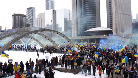 Toronto, OntarioCanada - February 27, 2022: Massive Torontonians wave Ukrainian flags and release blue and yellow smoke to protest against Russian invasion and condemn Putin on Nathan Phillips Square