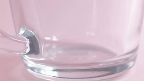 hot water is poured into a transparent cup on a pink background, super slow motion video