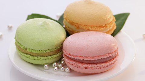 Close up of multicolor macarons , french macaroon, greedy pastry. French dessert sweets colored macaroons cookies arranged on a while plate rotating on white background