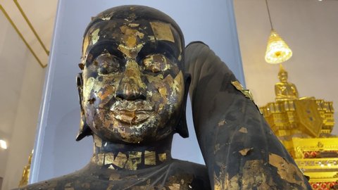 BANGKOK, THAILAND - Circa November, 2021: Gilded buddha statue with gold leaf for good merit and enlightenment in a buddhist temple - Close up shot with golden buddha statues in the background