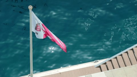 Monaco, Monte-Carlo, 08 July 2019: The flag of the new yacht club of Monaco in the wind in sunny weather, the water is azure in the background, the promenade of the port of Hercules