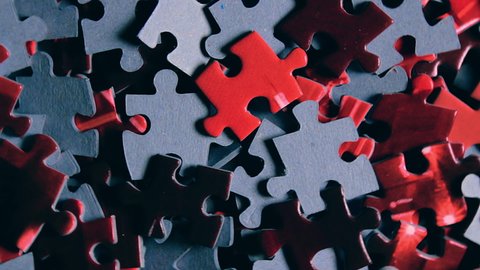 Background of Colored Puzzle Pieces that Slowly Rotating Counterclockwise - Top View, Close-Up. Texture of Incomplete Red and Grey Jigsaw Puzzle with Low Key Light - Left Rotation