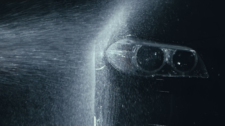 Car headlight wash. Washing modern vehicle body by high pressure jet wash hose water. Auto glass headlamp, angel eyes in drops. Close up of the spotlight of a black automobile as it gets cleaned. | Shutterstock HD Video #1087728473