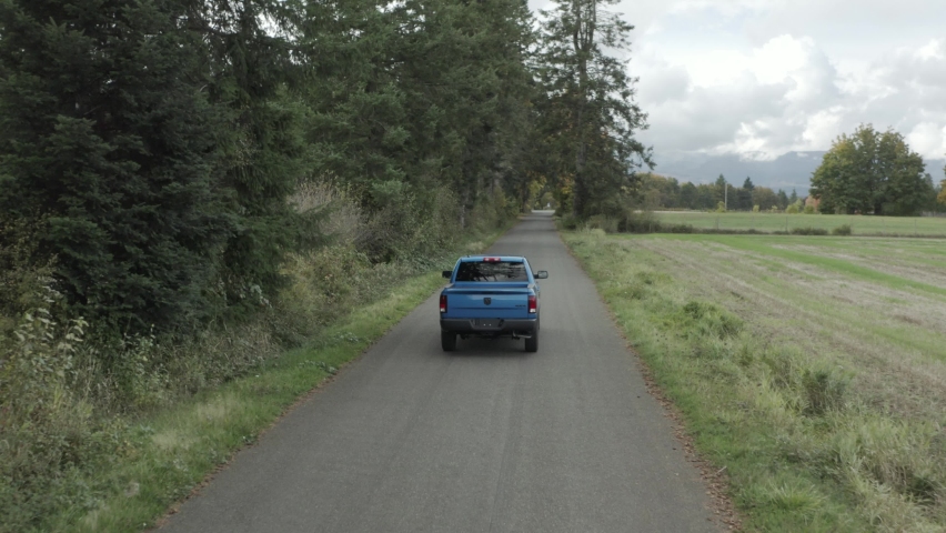 Blue RAM pickup truck driving along rural road. Aerial tracking Royalty-Free Stock Footage #1087730987