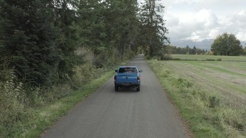 Blue RAM pickup truck driving along rural road. Aerial tracking