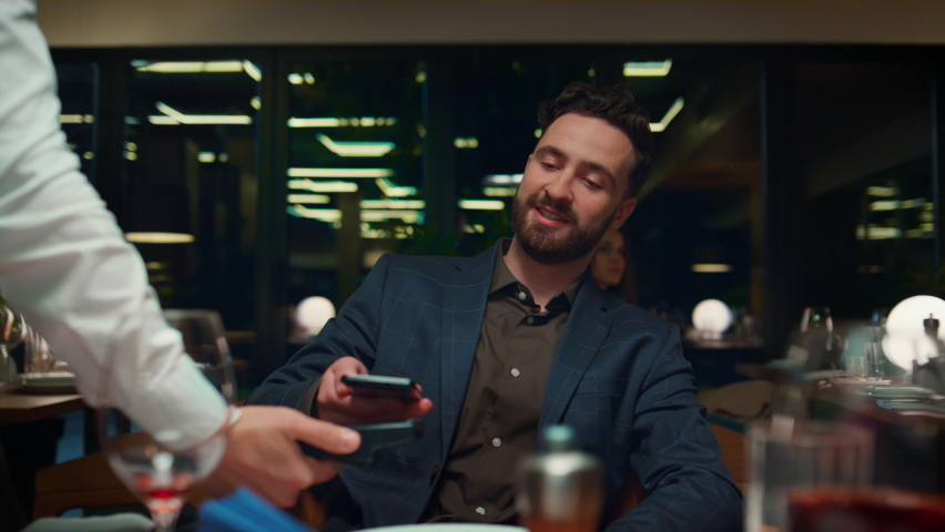 Man nfc paying dinner at fancy restaurant table. Happy businessman looking expensive bill in cafe. Handsome gentleman using mobile phone cashless contactless payment in eating place. Dining concept. | Shutterstock HD Video #1087731359