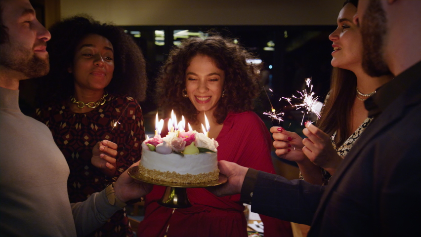 Birthday girl blowing cake burning candles on night restaurant party. Multiracial friends sing on festive celebration. Close up happy people group enjoying surprise event. Having fun together concept. | Shutterstock HD Video #1087731392