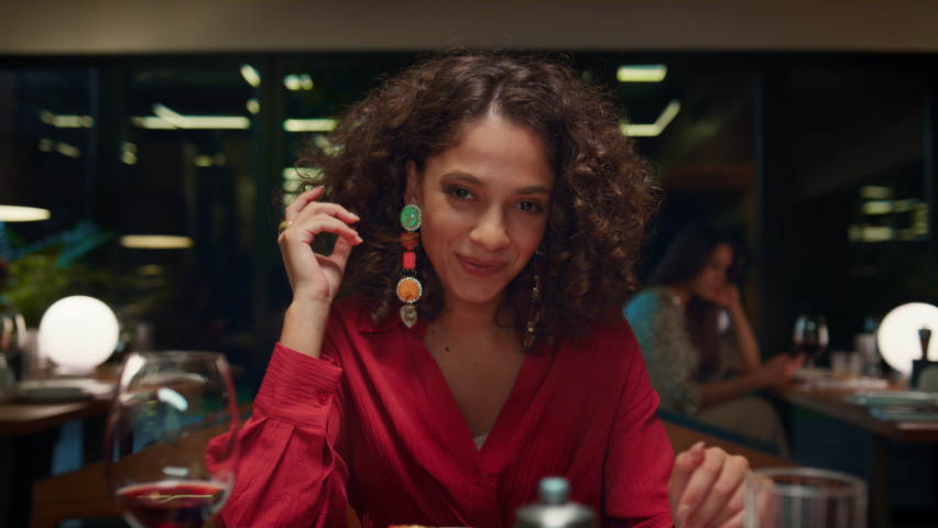 Laughing woman looking camera on romantic dinner date in fancy restaurant. Attractive african american girl smiling at cafe table. Young lady wearing beautiful dress in night bar. Fine dining concept.