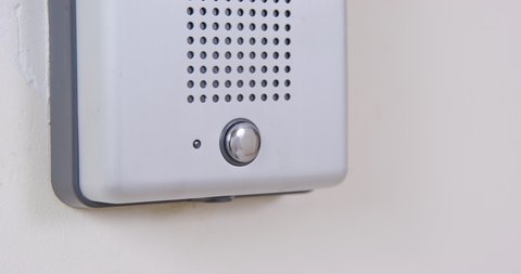 Person presses a doorbell, hanging on white wall, or an intercom call button with his finger, close up. Someone came to visit or to a private institution. Security systems for homes