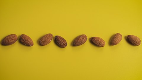 Almond seeds, rotating synchronously in a line on a yellow background. Concept of a coherent precise mechanism and a healthy diet. Stop-motion animation. 2D top view