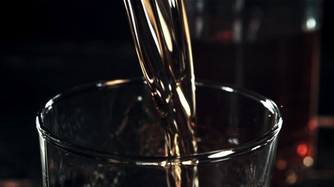 Cognac with splashes is poured into a glass. On a black background.Filmed on a high-speed camera at 1000 fps. High quality FullHD footage