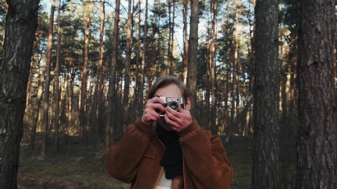 A young blond male photographer takes pictures of nature. Photographer takes pictures in the woods with a retro camera. Young photographer dressed in retro style. 