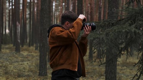A photographer takes pictures in the woods, a young man takes pictures in the woods with his camera. Beautiful nature through the eyes of a photographer. 