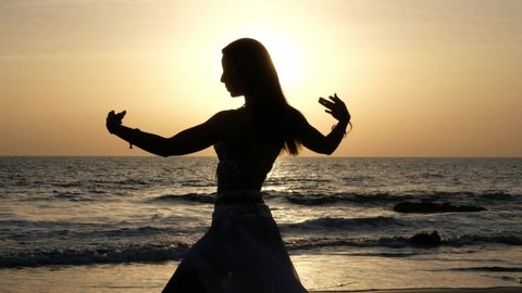 Silhouette of belly dancer woman dancing belly dance on a paradise beach at sunset