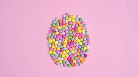 6k Colorful rainbow candies make Easter egg shape on bright pastel pink background. Stop motion flat lay concept	
