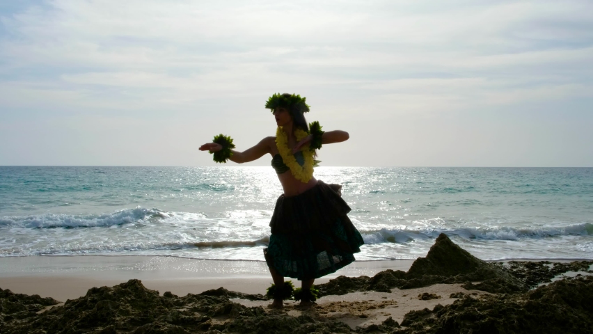 Woman performing Polynesian dances dressed in typical Hawaiian costume is dancing on the beach