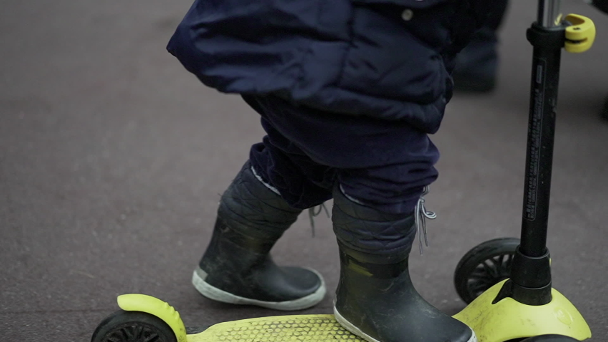 Close up toddler feet riding scooter outside in street