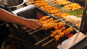 Local Asian Street food: Chef Cooking Traditional Thai Satay on Grill at Night Food Market. Phuket Town, Thailand. 4K Slowmotion High Quality Footage Video.