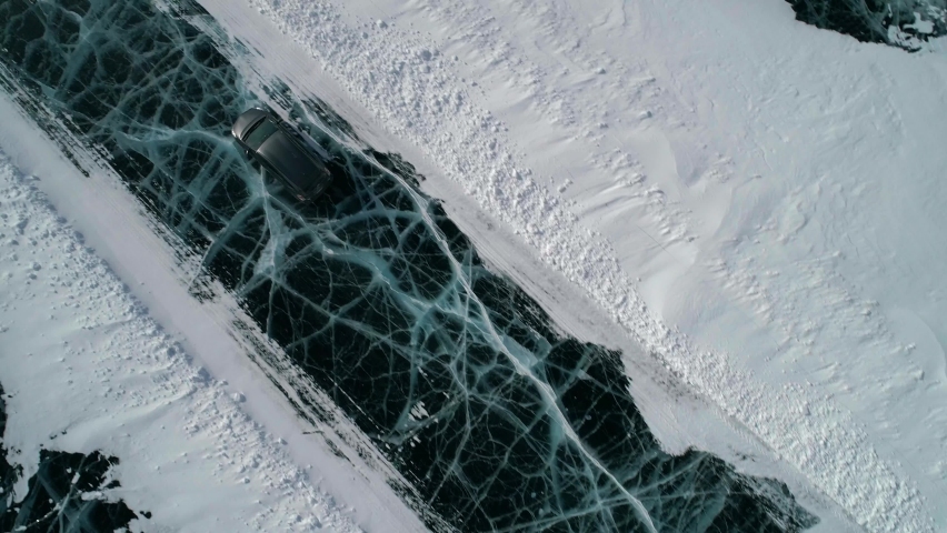 Aerial top down tilt view on a car driving on an ice road on frozen Baikal. Winter landscape of lake Baikal. Drone follows the car