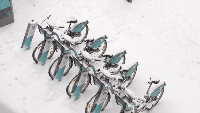 A man walks past rental bikes standing under a snowfall on a winter day.