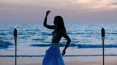 Beautiful belly dancer silhouette performing belly dance at the beach