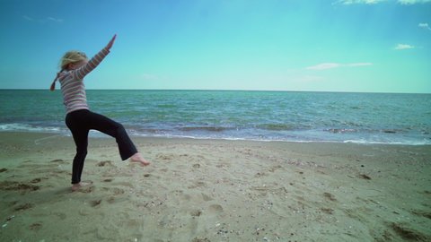 Little child girl making cartwheel acrobatic movement on a bach by the sea