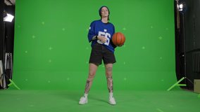 Girl wearing street hip hop style posing over green screen background. Young woman holding basketball ball on Chroma Key. 4k uhd video footage