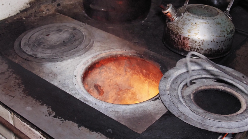 Man moves the fireplaces with the poker and places the dirty kettle on the stove in the rustic old kitchen stove.