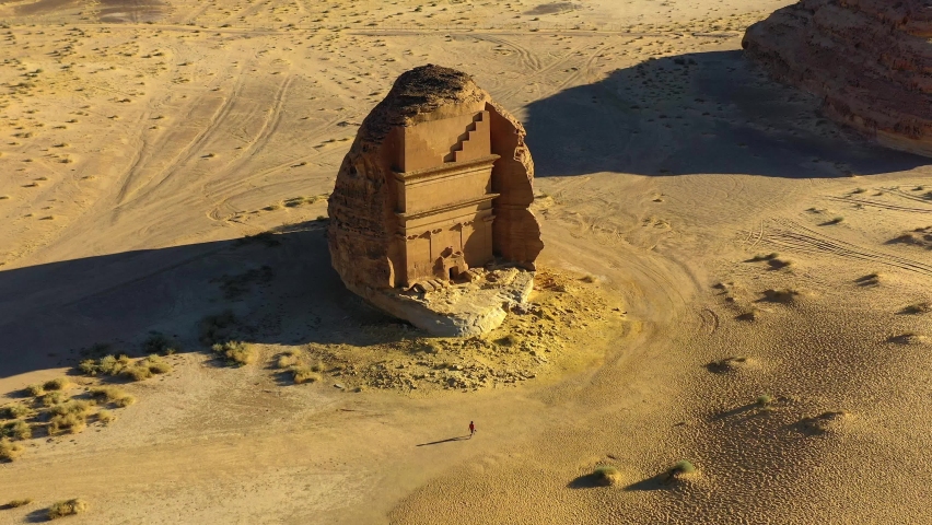 Aerial view of a person walking in front of the Hegra monument, golden hour, in Hejaz, Saudi Arabia - descending, drone shot Royalty-Free Stock Footage #1087763960