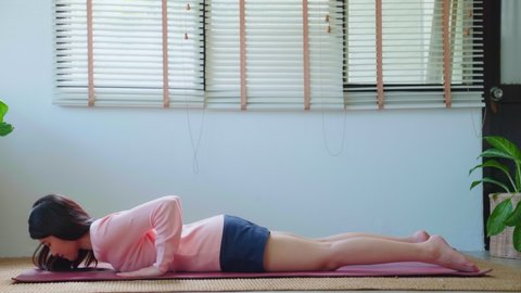 Attractive beautiful asian woman in casual doing yoga cobra pose at home. Body care morning routine at cozy living room interior indoor. reducing stress, Healthy lifestyle, Keeping in shape.