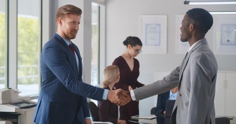 Business partners shaking hands in modern workplace office. MGroup of colleagues discussing contract and handshaking at meeting with colleagues talking on background