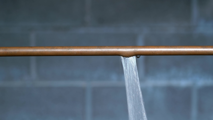 Water spraying from a thawed copper pipe that ruptured because it had frozen during the cold winter with a cinder block wall in the background. Royalty-Free Stock Footage #1087769579