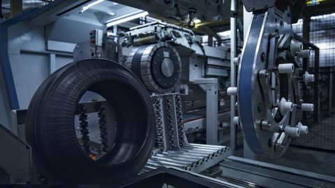 Tire on technological plant with modern industrial machine working automatically. Mechanical automated technology of tyre manufacturing at work in automotive warehouse. Factory indoors concept