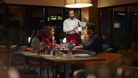 Waiter pouring wine bottle to fancy couple table at night restaurant dinner date. Two people celebrate anniversary on romantic dinner date at evening. Lovers taste alcohol together. Leisure concept. - Powered by Shutterstock - Get 15% off with code: PIKWIZARD15