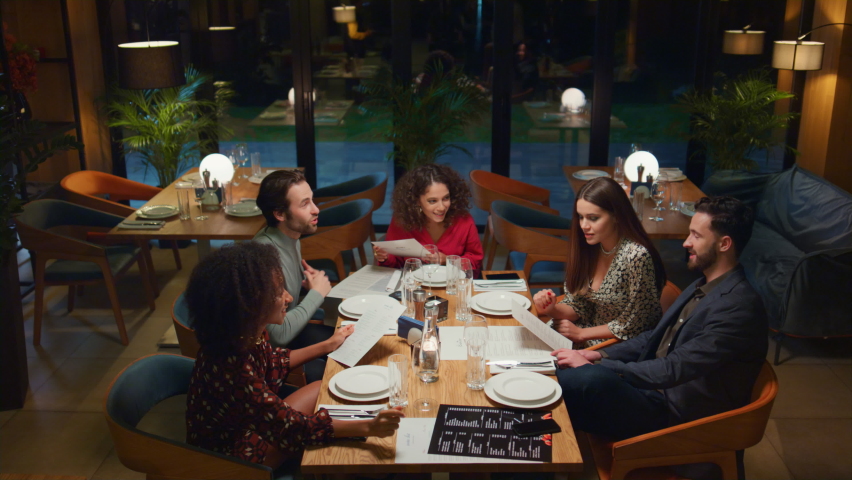 friends talking chatting together in fancy restaurant. Young people look menu at cafe table. Cheerful group choosing food in fine dining place. Meeting celebration leisure together concept. Royalty-Free Stock Footage #1087774733