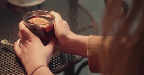 Cup of mulled wine and warming female hands holding steaming mug, outside closeup view