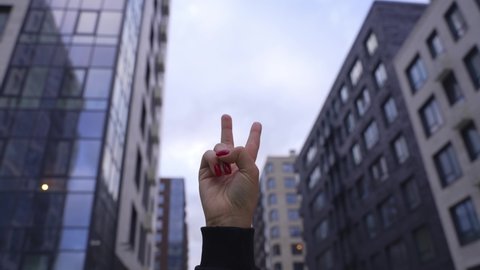Woman raising two fingers up and showing peace or victory symbol or letter V. Female one hand holding two fingers up in sign language on city background. No war concept