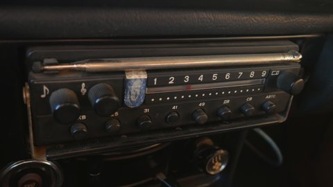 The old radio is tuned by turning the dial in the car. The radio dials the number, looks for stations. Old radio of the USSR. Human hand