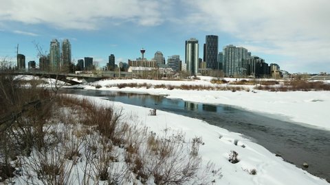 Moving drone shot of Calgary skyline with Bow River in foreground.  Winter