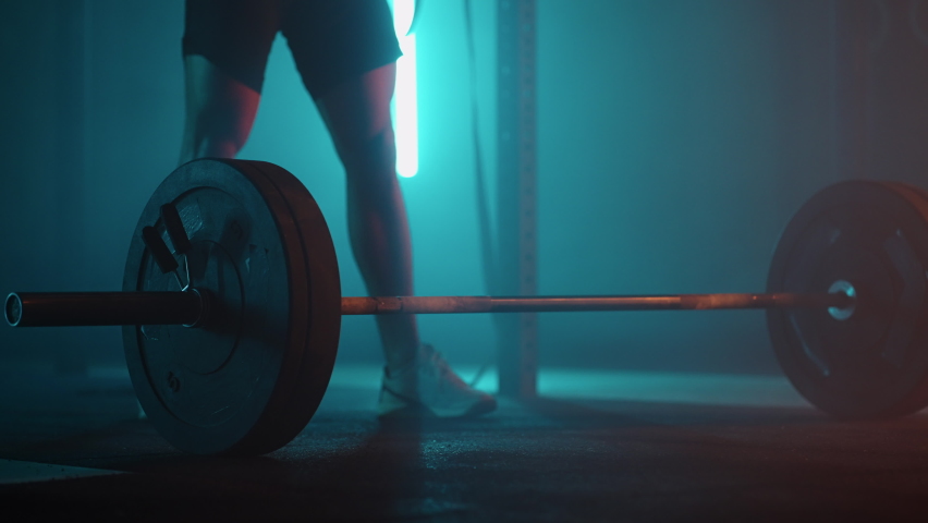 strong man is approaching to barbell in dark dramatic gym and lifting weight, legs of sportsman Royalty-Free Stock Footage #1087787390