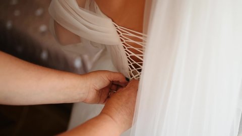 Bride's lace up dress. Bridesmaid tying bow on wedding dress. Woman's hands lace up silk ribbon on bride's corset. Helping to lace up. Beautiful bride in a white wedding dress. back woman view