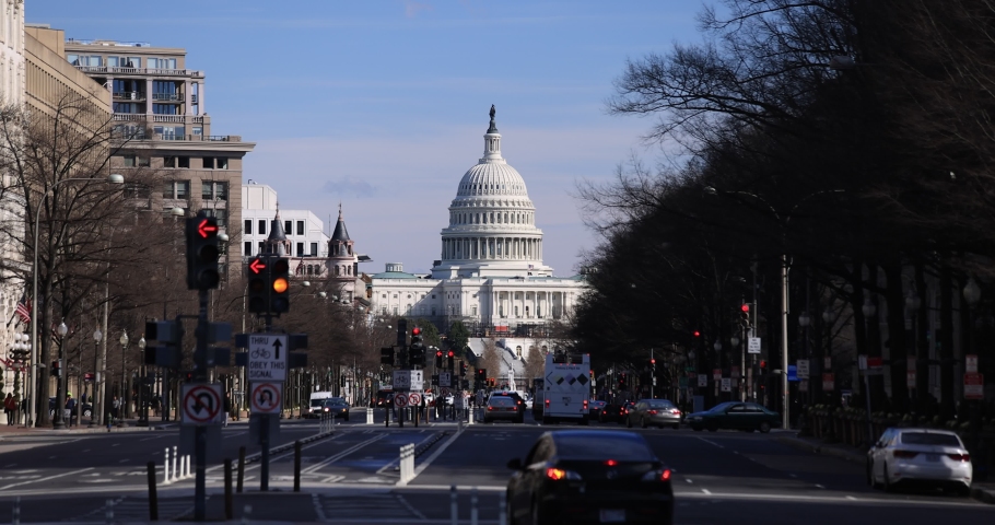 Slow-motion shot of the U.S. Capitol Building in Washington, D.C. seen from Pennsylvania Avenue on a winter afternoon. Vehicle traffic and pedestrians move around in the foreground.
