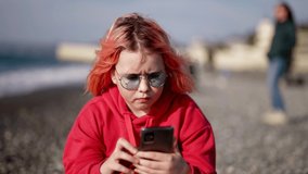 little girl is resting on seashore in city and playing video game in smartphone