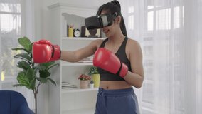 Healthy Asian athletic woman in sportswear is having fun playing games or practicing boxing with virtual reality glasses in her home.