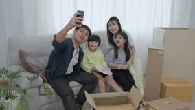 family parent and little daughter and son relax on sofa in living room on new home and take selfie with smartphone together with smiling and cheerful laugh.