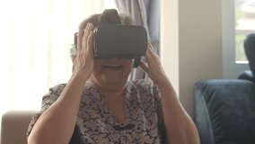 Happy senior woman using VR Headset virtual reality simulator in a living room