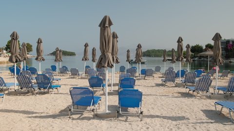 Beautiful beach with umbrellas and sunbeds at Ionian sea in Ksamil, Albania. Perfect summer vacation destination. Sunshades and sunbeds on the empty beach. Slow steadicam footage