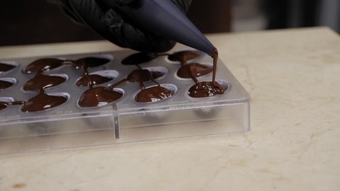 A woman pastry chef fills a candy mold with melted chocolate using a pastry bag in a professional kitchen. Cooking handmade chocolates.