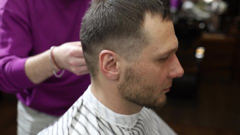 Close-up of hair cutting with a trimmer on the head of a customer with pink hair. The master barber in black gloves carries out a quality haircut in an authentic barbershop. Macro slow motion.