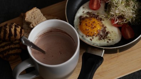 Closeup of woman having breakfast of hot chocolate and scrambled egg. Dip piece of bread in yolk